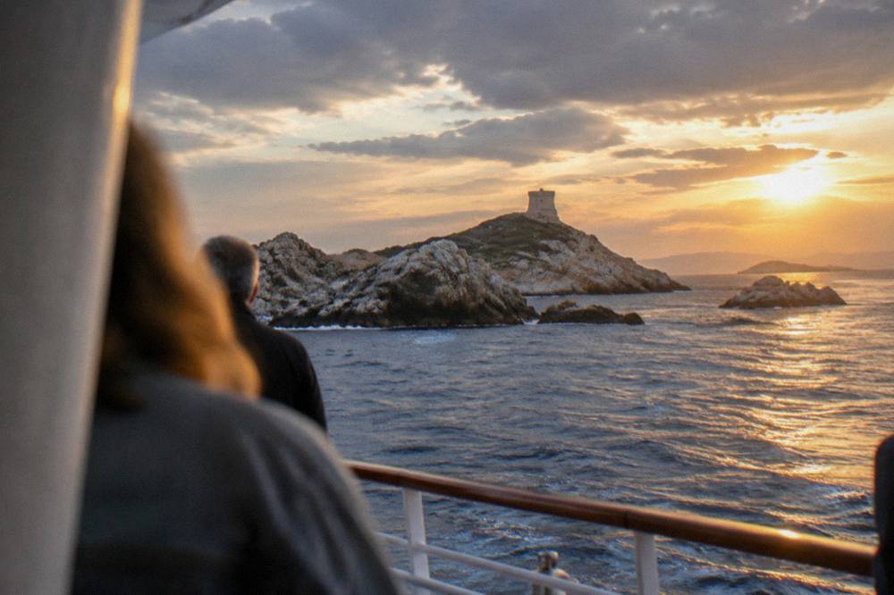 Passengers on a boat deck passing close to rocky islets in the late afternoon