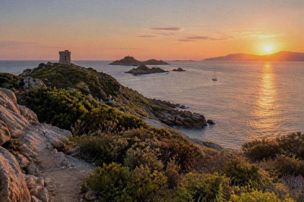 The sun setting over a Mediterranean gulf with islands on the horizon seen from the water