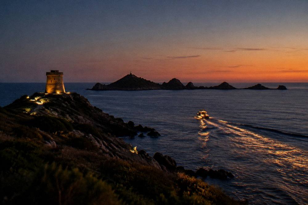 A boat wake catching golden light as a vessel heads back towards a harbour at dusk