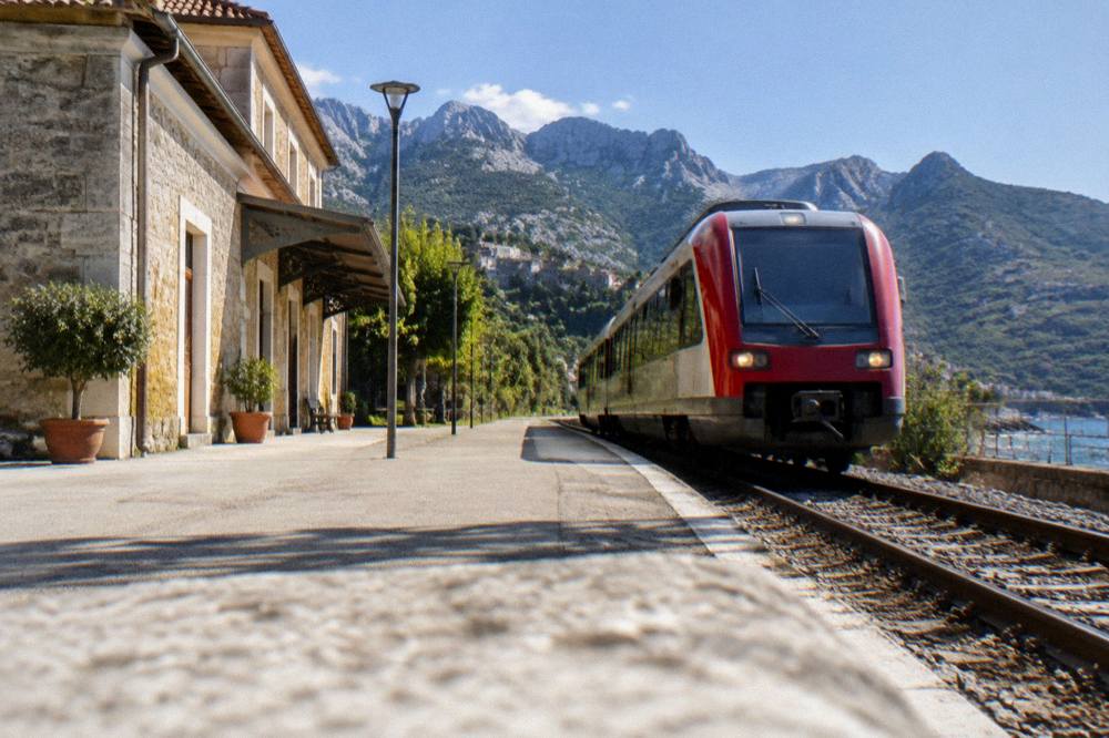 A red and white Corsican train arriving at a coastal station at golden hour