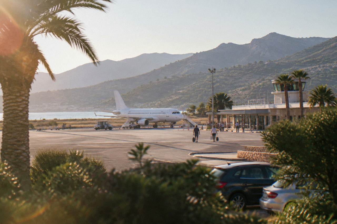 Aircraft parked at a small Mediterranean airport terminal with dry hills behind