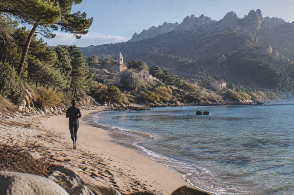 A sandy Corsican beach with clear shallow water and a few pines at the edge