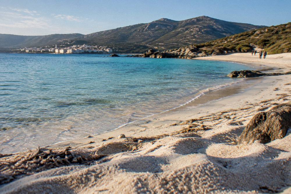 White buildings of a Corsican harbour town seen across a bay in evening light