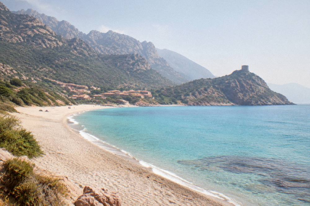 Aerial view of a turquoise bay with a long sandy beach and a small town in northwest Corsica