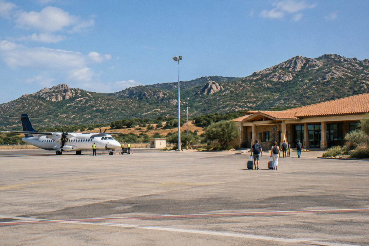 A small airport building on a Corsican coastal plain with wooded hills rising behind it
