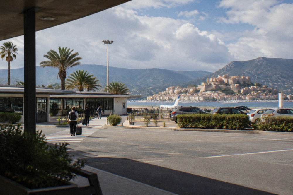 A white town built around a bay with a citadel and yacht masts along the waterfront