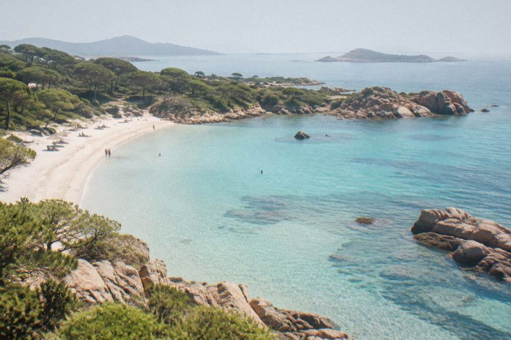 Aerial view of a turquoise cove with pale sand and granite headlands