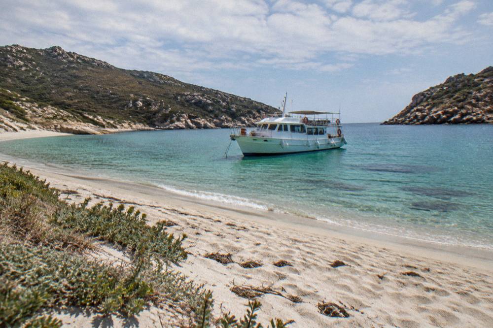 A white passenger boat moored near a Corsican beach with rocky headlands on both sides