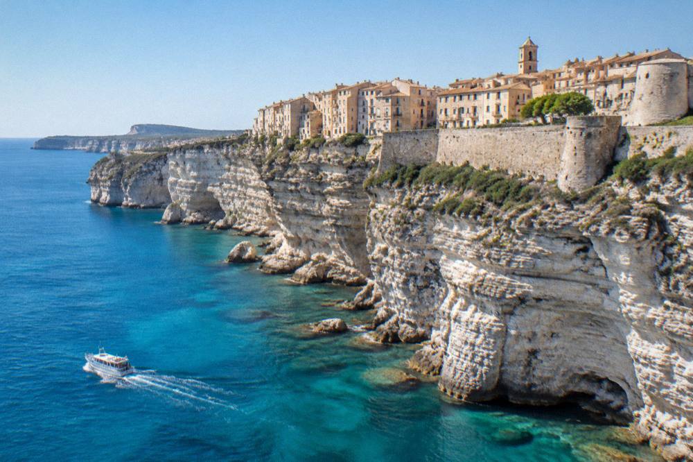 Tall white limestone cliffs above the sea at Bonifacio with a boat passing below