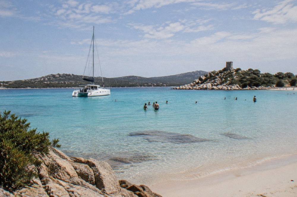 A catamaran anchored off a Corsican beach with swimmers in the shallows