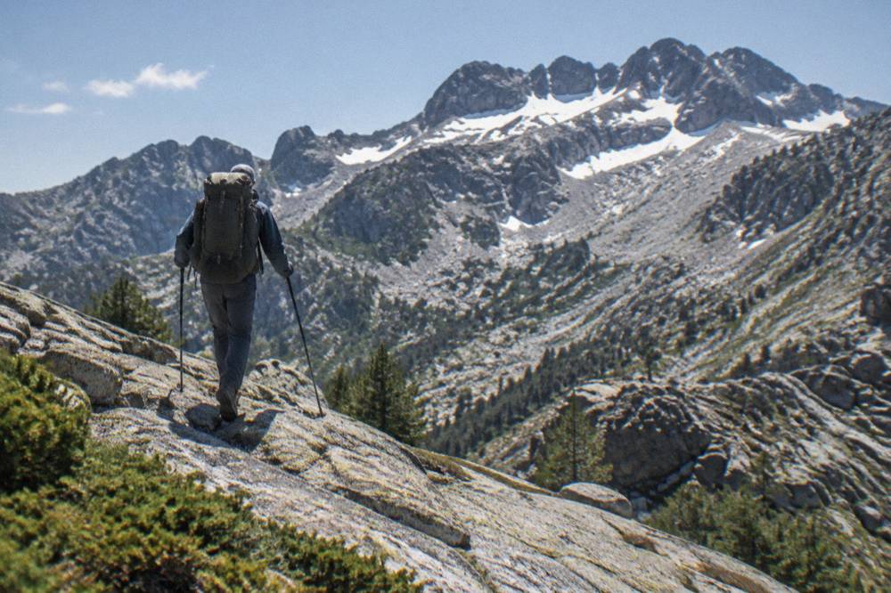 A walker with a large backpack crossing a granite slope near a ridge line