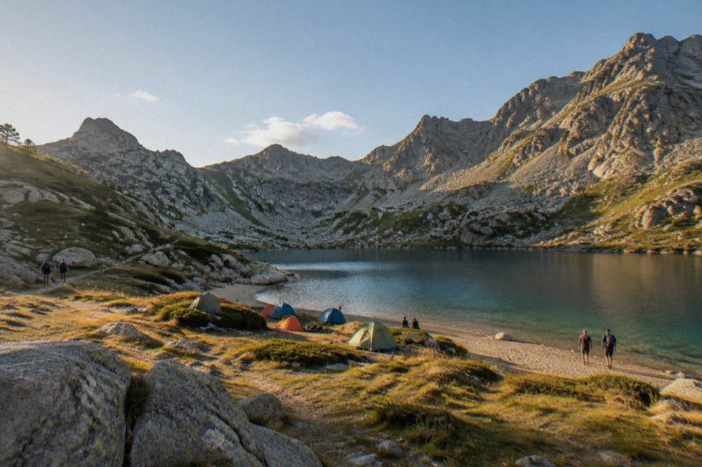 A campsite of small tents near a sandy beach with clear water beyond