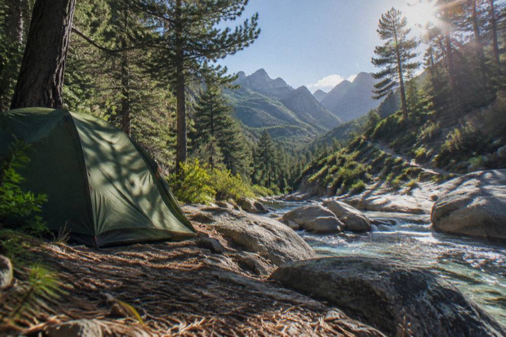 A tent beside a river in a green mountain gorge with pine trees