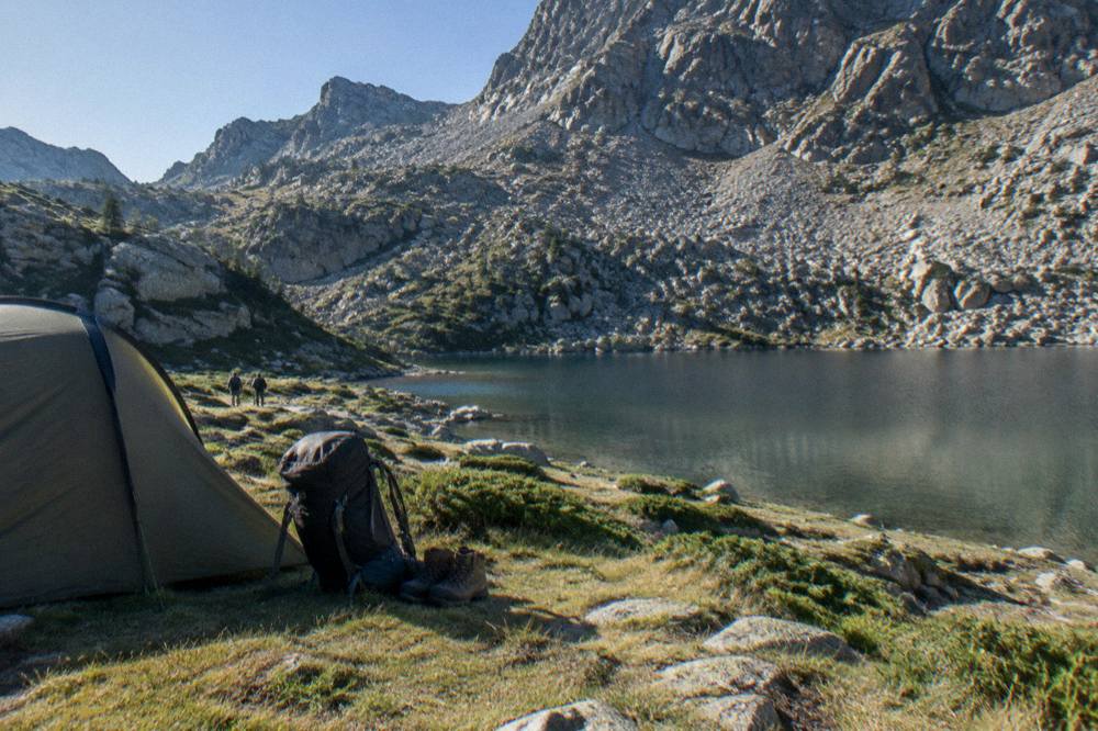 A backpack and hiking boots resting beside a tent at sunrise