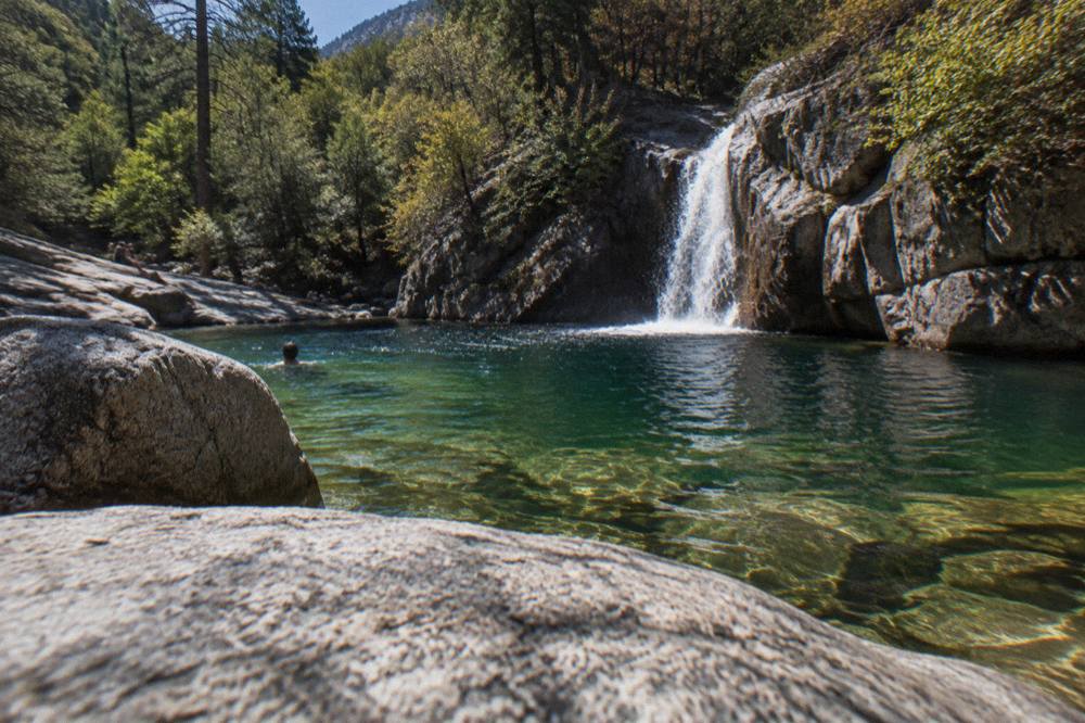 A waterfall dropping into a deep green pool inside a forested Corsican gorge