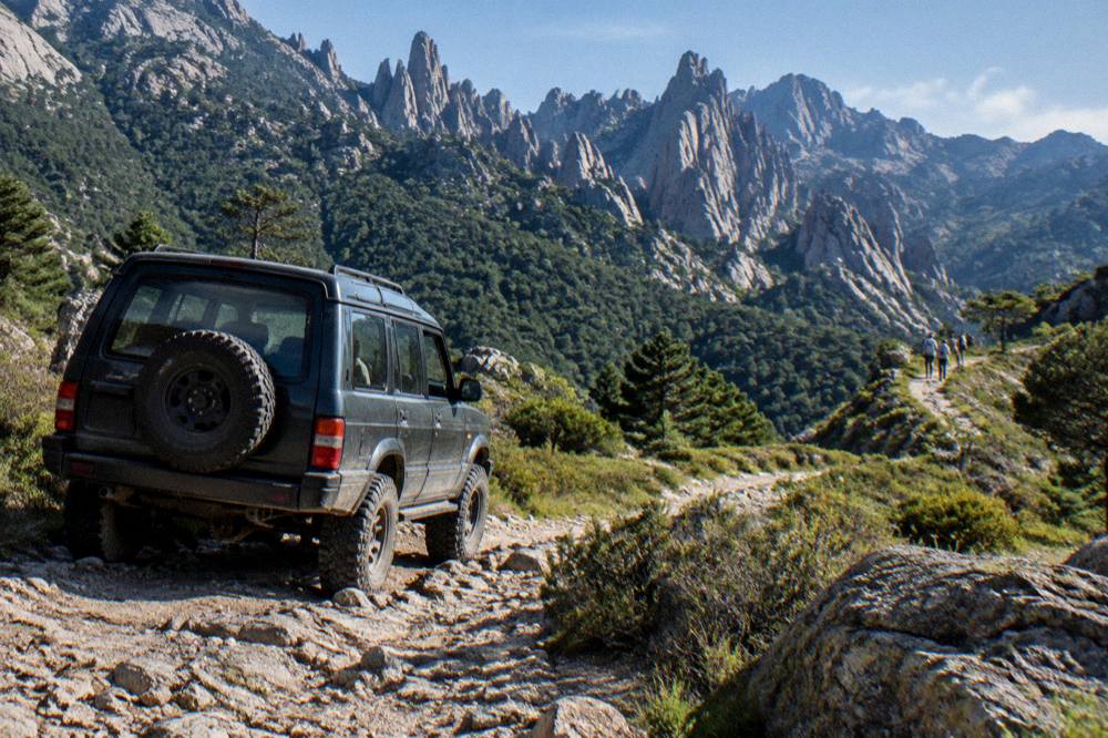 A four-by-four vehicle on a rocky mountain track high above forested Corsican slopes