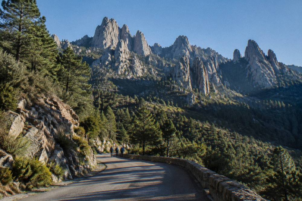 A winding mountain road climbing through Corsican forest toward granite peaks