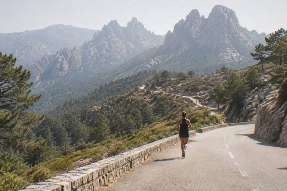 A hairpin road climbing through pine forest toward bare granite peaks in the Corsican mountains
