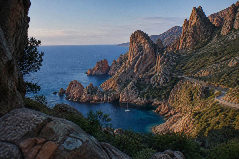 A red rock inlet with a small boat anchored in clear water near the Calanques de Piana