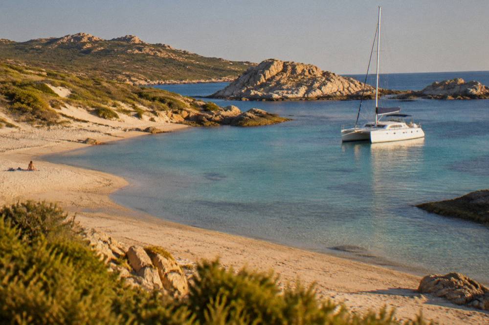 A white catamaran moored above clear shallow water near granite islands off Corsica