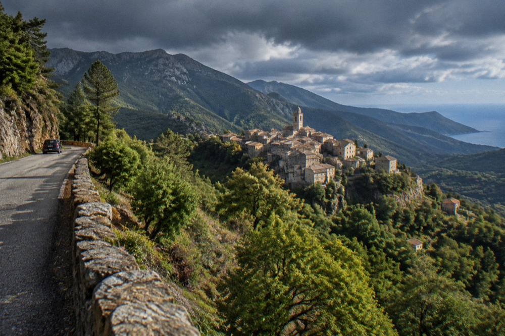 Sunlight over a mountain road with dark storm clouds above the Corsican peaks