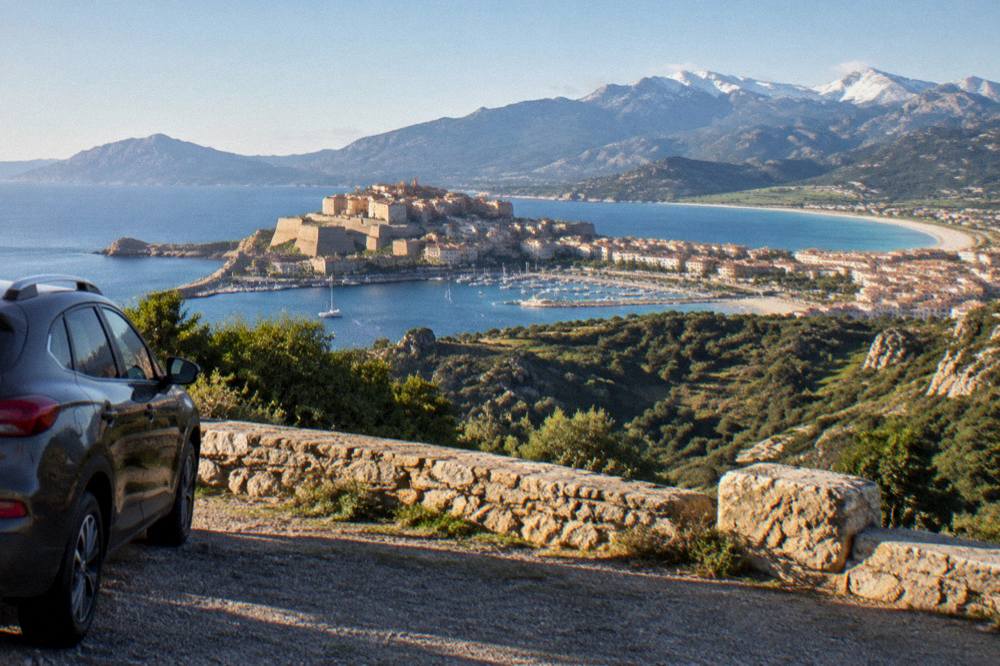 A parked car at a viewpoint overlooking a deep green mountain valley in central Corsica