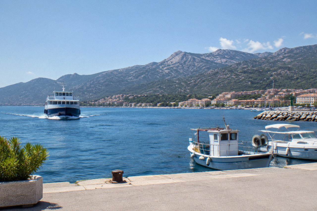 A ferry approaching a Corsican harbour with mountains rising behind the town