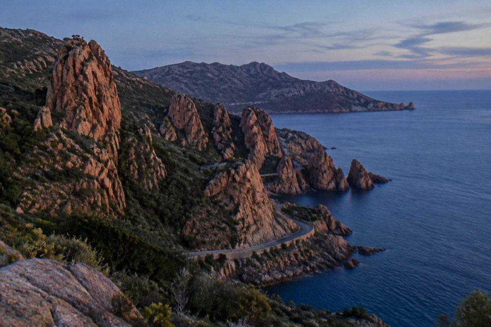 Red granite rock formations of the Calanques de Piana rising above calm sea