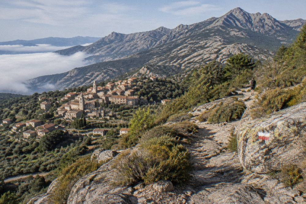 A ridge trail marked with red and white paint across bare granite above a cloud-filled valley