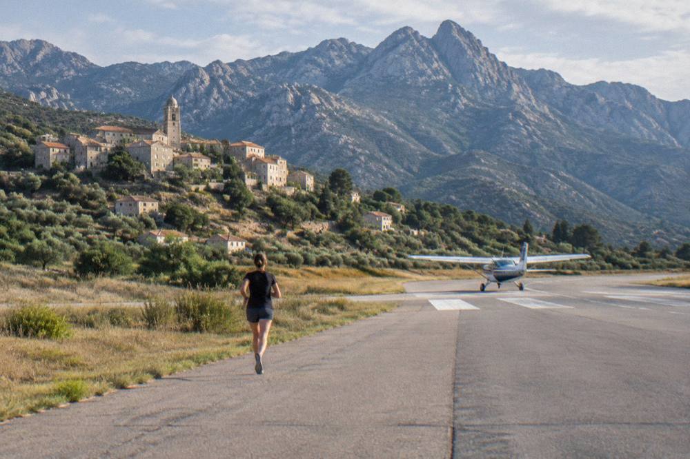 A small aircraft on a regional airfield runway with mountains in the background