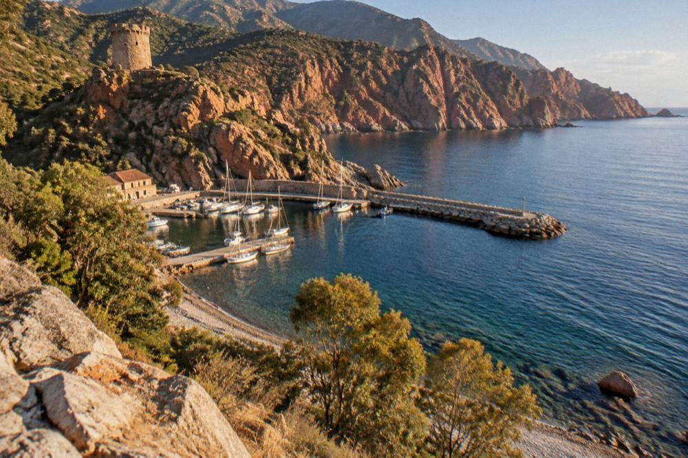 Red granite cliffs rising from clear water along the Gulf of Porto coast