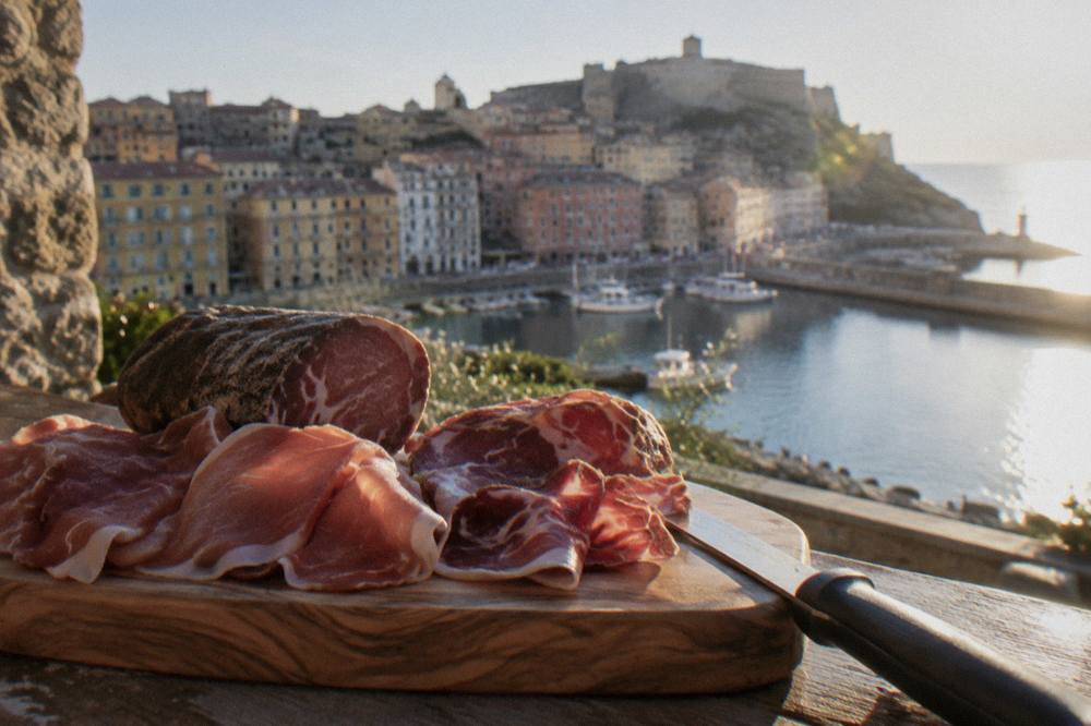 Slices of Corsican cured ham and coppa arranged on a wooden board next to a knife
