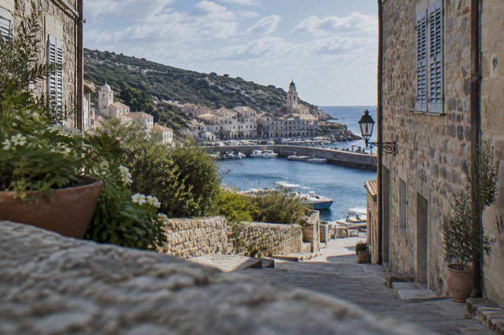 A narrow shopping street in a Corsican town with stone buildings and shutters