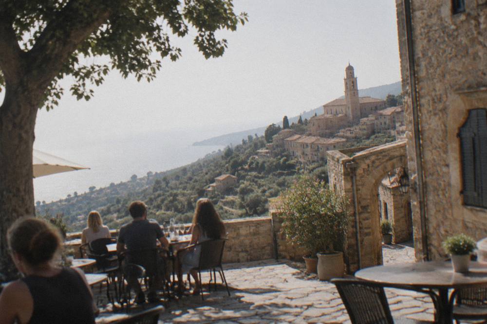 People seated at outdoor tables on a Mediterranean seaside square in the early evening