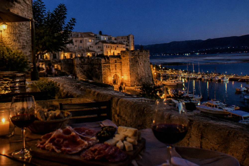 A table set with charcuterie slices, cheese and glasses of red wine at dusk