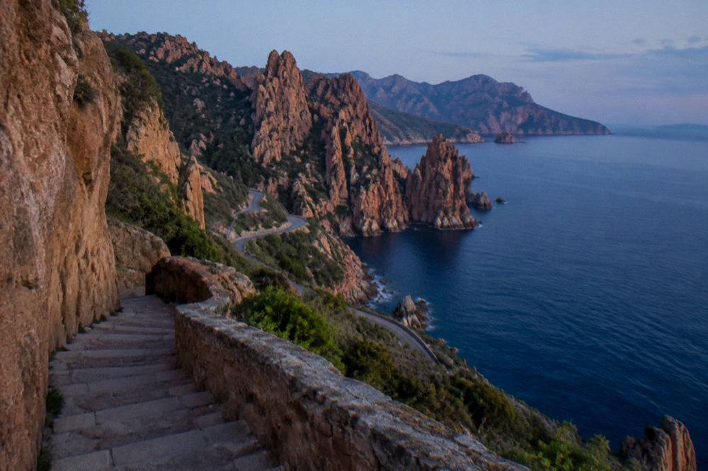 A stone stairway cut into a cliff face leading down toward the sea at golden hour