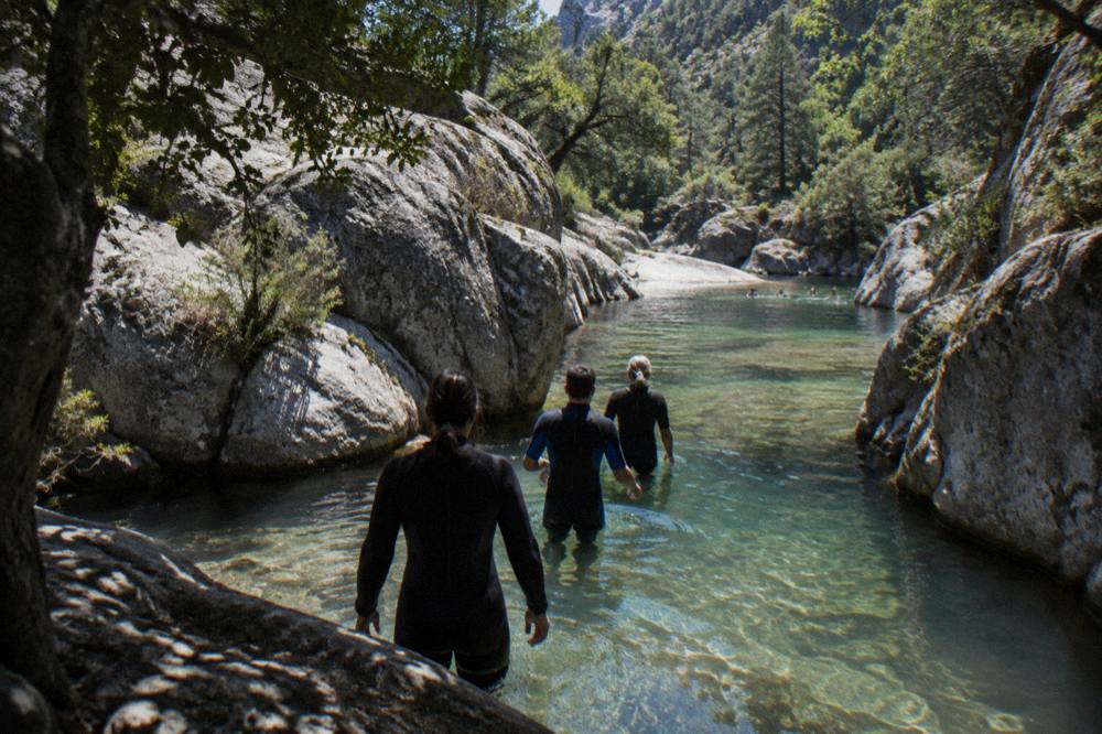 A wetsuit-clad group wading through a narrow rocky canyon with clear water