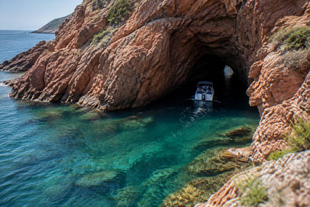 A small boat entering a sea cave in red rock on the Corsican west coast