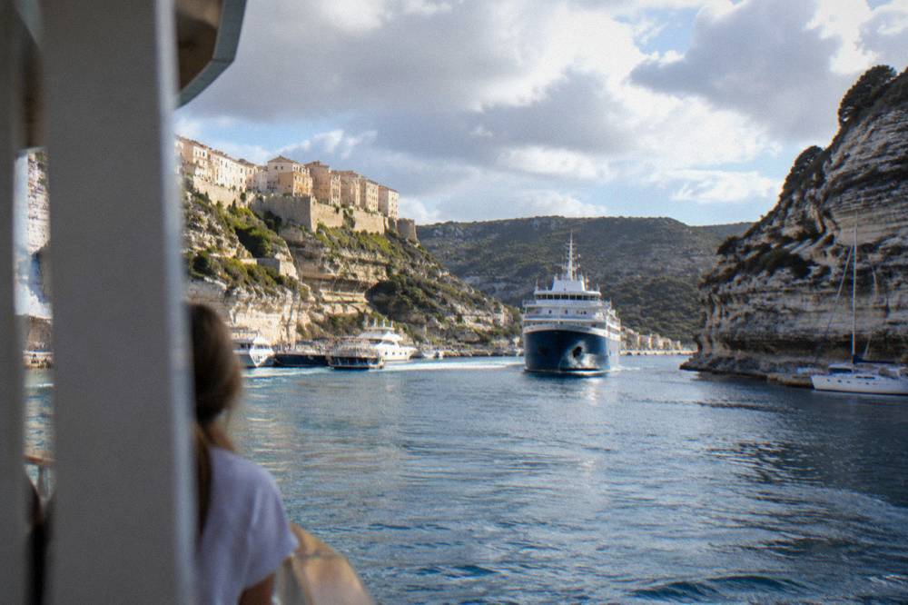 A large ferry approaching a Corsican harbour town with hills behind