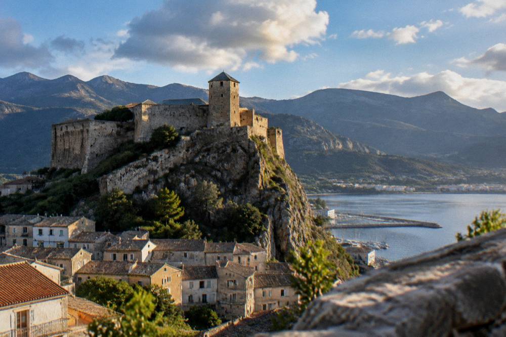 The ramparts of a Corsican citadel above a harbour at golden hour