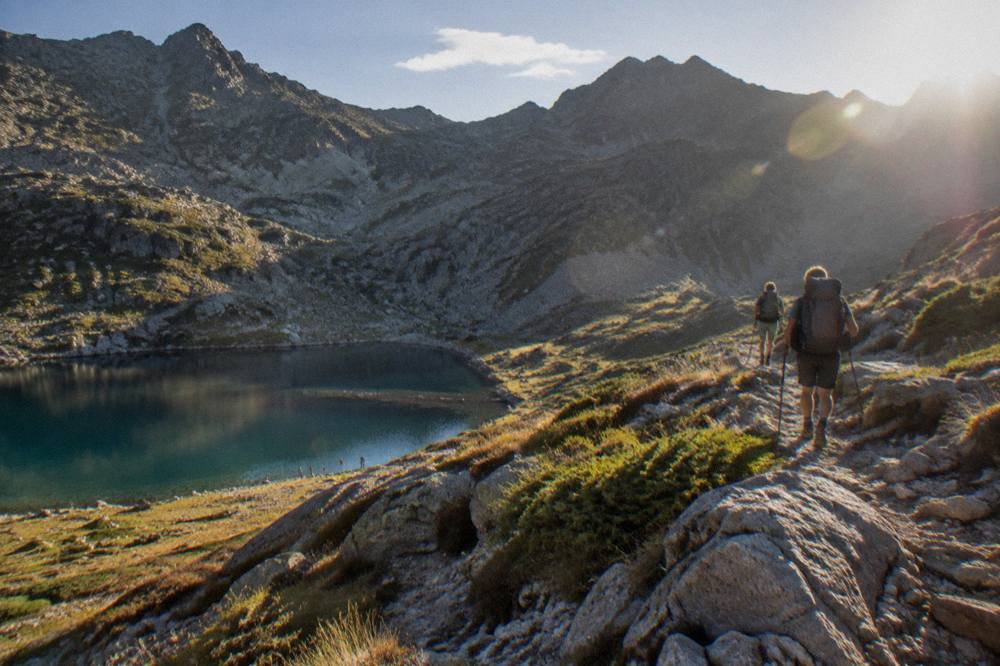 Hikers with backpacks on a rocky mountain ridge path above clouds in Corsica