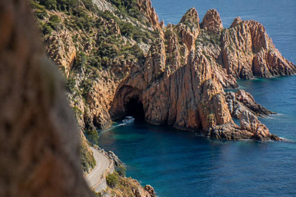 A small boat entering a red rock sea cave along the Corsican coast