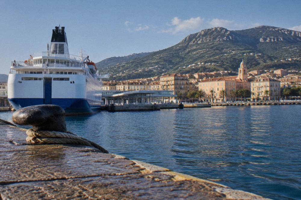 A ferry approaching a Corsican harbour town at the foot of hills