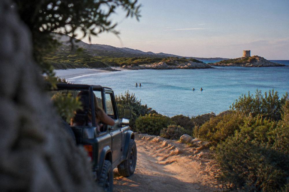 An open-top 4x4 driving a dusty track between maquis hills in Corsica