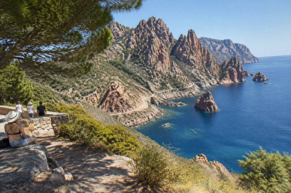 Red granite cliffs above clear water on the Corsican west coast under a cloudless blue summer sky