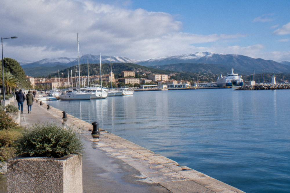 A Corsican coastal town waterfront in winter under a mixed sky with calm water in the harbour