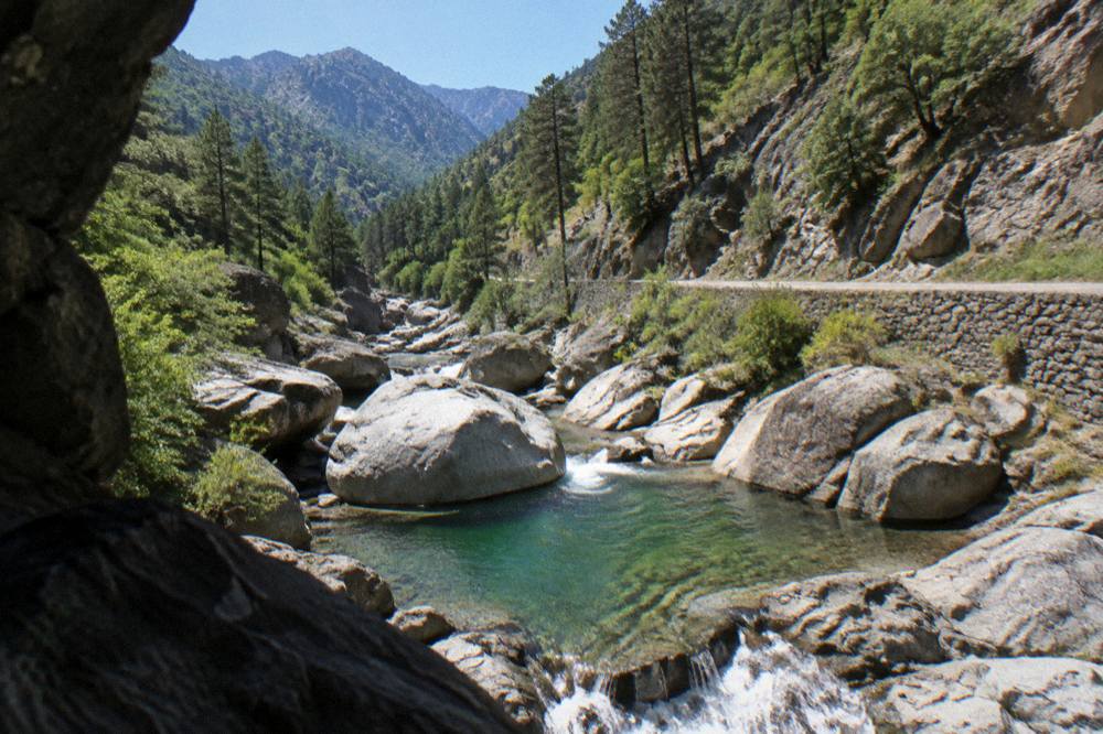 A deep mountain valley in the Corsican interior with a river running between forested slopes