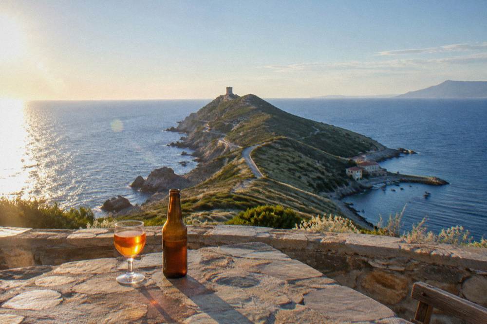 A small glass of amber aperitif and a bottle of local beer on a stone terrace table