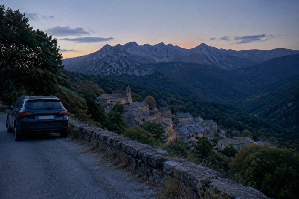 A car parked on a mountain road above a hilltop village in the Corsican interior
