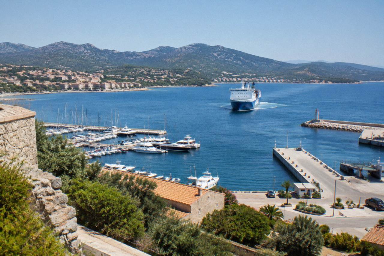 A car ferry approaching a Corsican harbour town with hills behind it